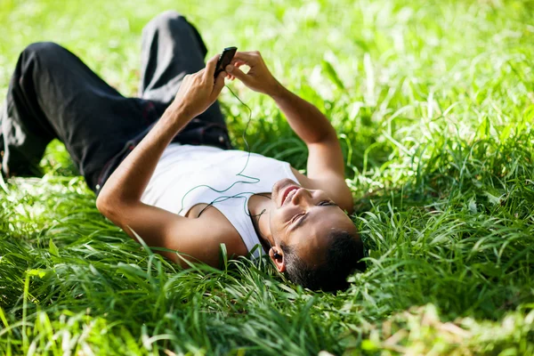 Glad kille ligga på gräset och lyssna på musik — Stockfoto