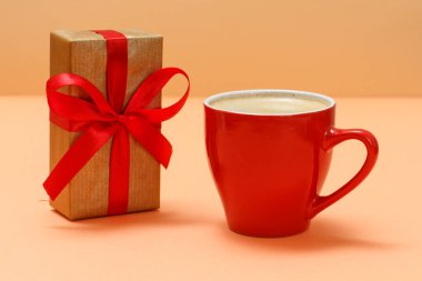 Bej arka planda bir fincan kahve ile kırmızı hediye kutusu.
