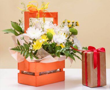 Tahta sepetin içinde bir buket sarı ve beyaz çiçek ve hediye kutusu..