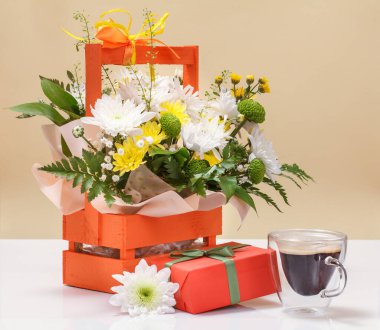 Tahta sepetin içinde bir fincan kahve ve hediye kutusuyla güzel sarı ve beyaz çiçekler..