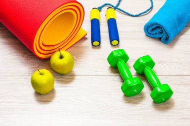 Yoga paspası, spor aleti, havlu, elma ve dambıllar bir odada ya da gri zeminde spor salonu..