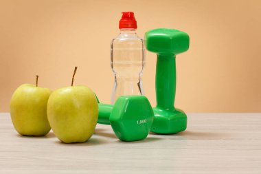Fitness için dambıllar, bej arka planda bir şişe su ve elma..