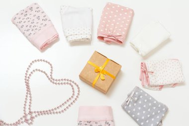 Farklı renklerde katlanmış pamuk külotlar, bir hediye kutusu ve beyaz arka planda boncuklar. Kadın iç çamaşırı seti. Üst görünüm.