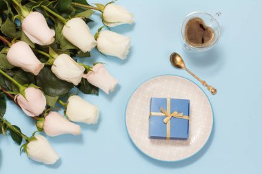Hediye kutusu ve mavi arka planda güzel beyaz güller olan bir fincan kahve. Tatillerde hediye verme kavramı. Üst görünüm.