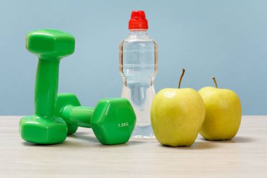 Spor için dambıllar, elmalar ve mavi arka planda bir şişe su..