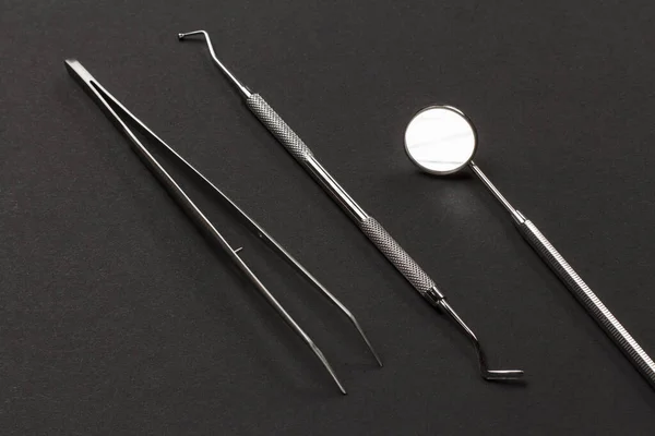 Set of metal instruments for dental treatment. Tweezers, a plugger and a mouth mirror on the black background. Medical tools. Top view.