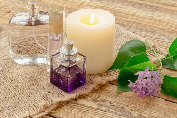 Garrafas de perfume, vela e flores lilás em fundo de madeira. — Fotografia de Stock
