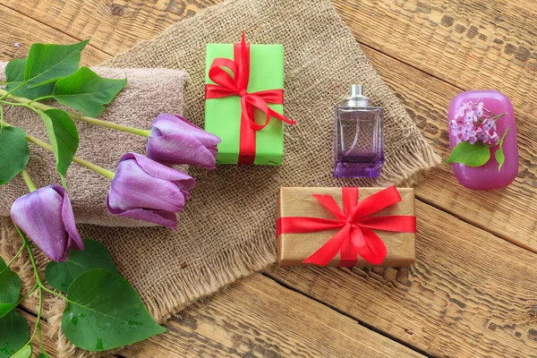 Ręczniki, prezenty, perfumy i kwiaty lilii na drewnianym tle. — Zdjęcie stockowe