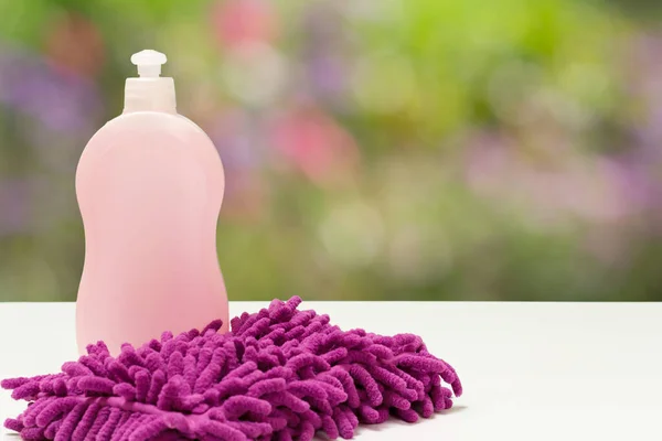Bottle of dishwashing liquid and a rag on the blurred natural background. Washing and cleaning concept.