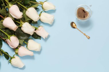 Bir fincan kahve ve mavi arka planda güzel beyaz güller olan bir kaşık. Tatillerde hediye verme kavramı. Üst görünüm.