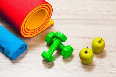 Yoga paspası, havlu, elmalar ve dambıllar bir odada ya da gri zeminde bir spor salonu.