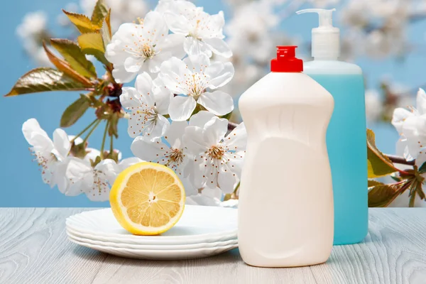 Botellas de líquido lavavajillas, platos y limón sobre fondo natural. — Foto de Stock