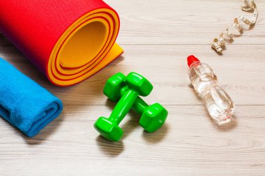 Yoga paspası, havlu, bir şişe su, bir mezura ve bir odadaki dambıllar ya da gri zemindeki bir spor salonu..