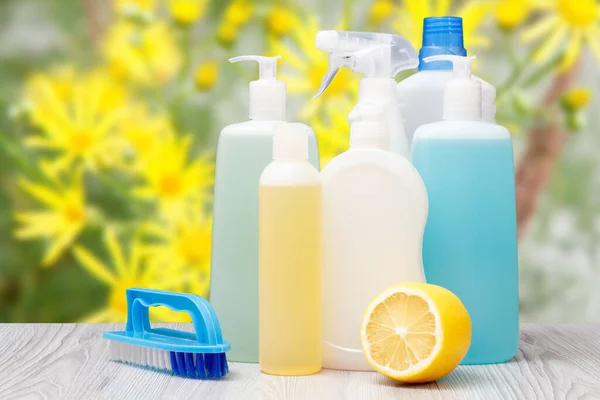 Plastic bottles of dishwashing liquid, glass and tile cleaner, detergent for microwave ovens and stoves, brush and lemon on the blurred natural background. Washing and cleaning concept.