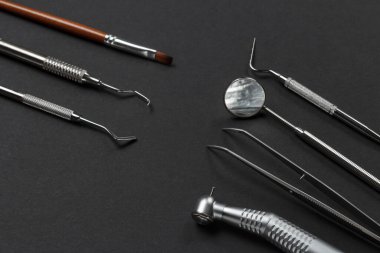 Yüksek hızlı diş teli, ama cımbız, ağız aynası ve tıkaçlı. Diş yenileme aleti, bir curette ve siyah arka planda bir fırça. Tıbbi aletler. Üst görünüm.