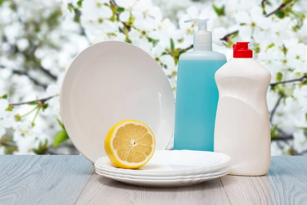 Bottles of dishwashing liquid, plates and lemon on natural background.