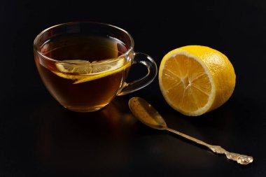 Bir bardak limonlu çay, siyah arka planda bir kaşık..