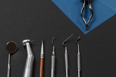 Ağız aynası, diş macunu, fırça, küret, tıkaç, diş yenileme aleti ve siyah arka planda kauçuk baraj pensesi. Tıbbi aletler. Üst görünüm.