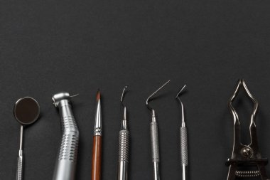 Ağız aynası, diş macunu, fırça, küret, fiş, dişçi yenileme aleti ve siyah arka planda kauçuk baraj kıskacı. Tıbbi aletler. Üst görünüm.