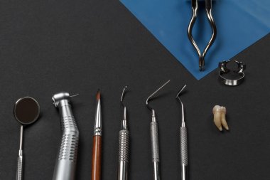Ağız aynası, diş teli, fırça, küret, tıkaç, dişçi yenileme aleti, kıskaçlı kauçuk pense ve çıkarılmış hasta bir diş. Tıbbi aletler. Üst görünüm.