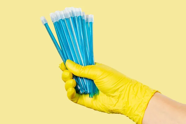 Dentist's hand in a latex glove with saliva ejectors on yellow. Medical tools concept.