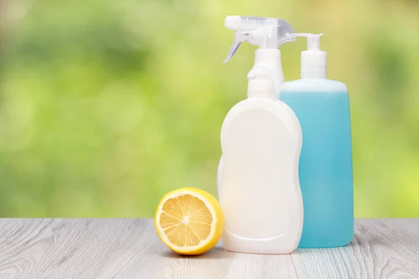 Plastic bottles of dishwashing liquid and a lemon on the blurred natural background. Washing and cleaning concept.