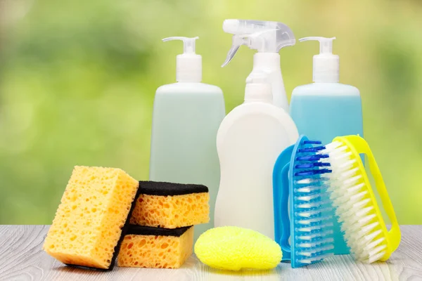 Plastic bottles of dishwashing liquid, glass and tile cleaner, detergent for microwave ovens and stoves, brushes and sponges on the blurred natural background. Washing and cleaning concept.