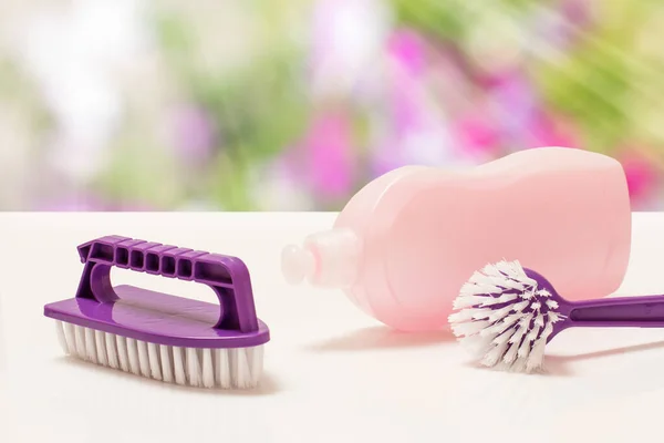 Bottle of washing liquid and plastic brushes on the blurred natural background. Washing and cleaning concept.