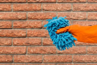 Close-up view of woman's hand in rubber protective glove with rag and a brick wall on the background. Cleaning concept.