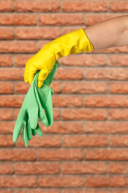 Close-up of woman's hand in a yellow rubber glove holding green ones with a brick wall on the background. Protection products for homework.
