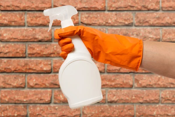 女用手戴着橙色防护手套 后面是玻璃瓶清洗液和砖墙 清洗及清洁概念 — 图库照片