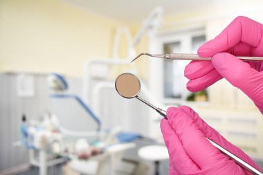 Dentist's hands in pink rubber gloves with a probe and mouth mirror with a dental clinic on the background. Medical tools concept. Top view.