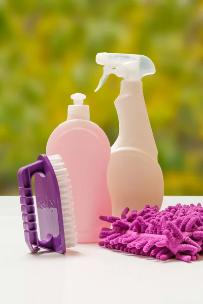 Bottles of washing liquid, a brush and a rag with blurred autumn leaves on the background. Washing and cleaning concept.