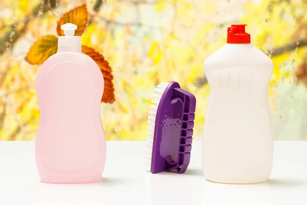 Bottles of dishwashing liquid and a brush on the blurred natural background. Washing and cleaning concept.