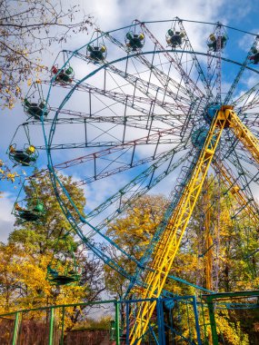 Ferris wheel with yellow trees and blue sky on the background in autumn day.