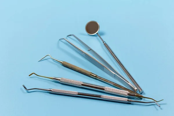 Mouth mirror, the tweezers, the dental restoration instrument, the curette and the plugger on the blue background. Medical tools.