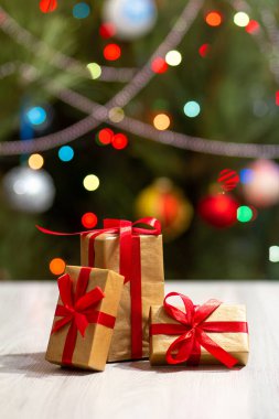 Kırmızı fiyonklu hediye kutuları. Arka planda parıldayan parti ışıkları ve oyuncak topları olan bir Noel ağacı. Noel kutlaması.