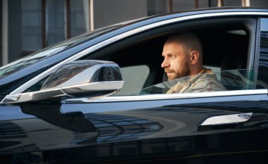 Siyah araba kullanan, sakallı, kendinden emin bir adam..