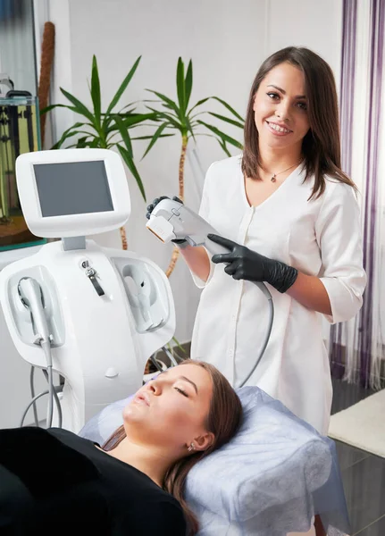 Hezký kosmetik s ultrafialovým zařízením stojící vedle pacienta na klinice. — Stock fotografie