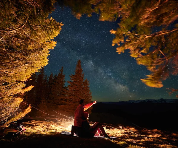 Man resenär visar stjärnhimmel till flickvän i bergen nära elden. — Stockfoto