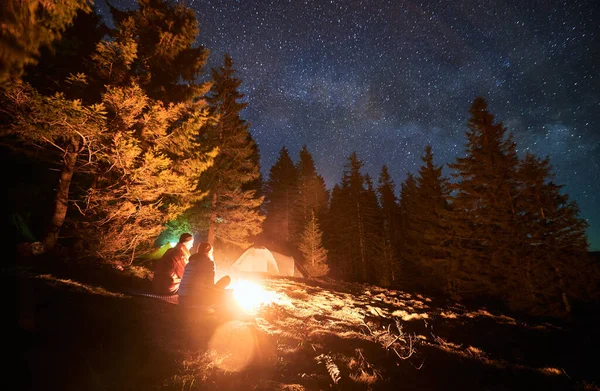 Urlauberpaar sitzt am Lagerfeuer unter Sternen. — Stockfoto