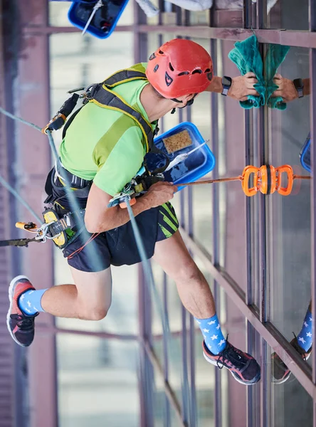 Endüstriyel dağcılık işçisi binanın penceresini temizliyor..