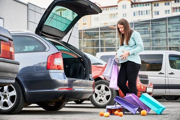 Scared pregnant girl looking at scattered bags of fruit in parking lot.