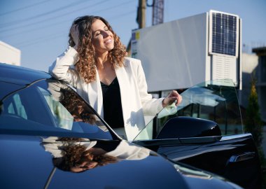 Arabanın yanındaki bayan şarj istasyonuna karşı güneş ışınlarının keyfini çıkarıyor..