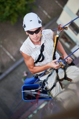 Endüstriyel dağcılık işçisi binanın penceresini temizliyor..