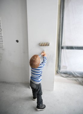 Renkli süveter giyen, fırça tutan ve duvar boyayan çocuk..