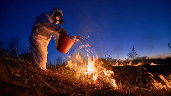 Fireman ecologist extinguishing fire in field in the evening