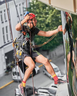 Endüstriyel dağcılık işçisi binanın penceresini temizliyor..