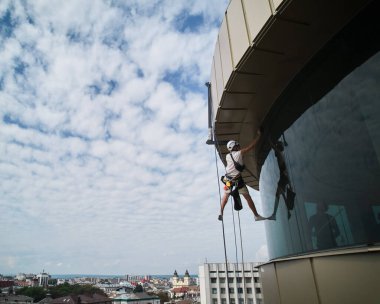 Endüstriyel dağcılık işçisi binanın penceresini temizliyor..