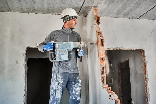 Trabalhador masculino na parede de perfuração de capacete de construção com broca de martelo. — Fotografia de Stock